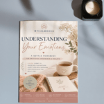 A thin printable workbook titled Understanding Your Emotions lying on a table next to a lit candle, cozy mug, and journal.